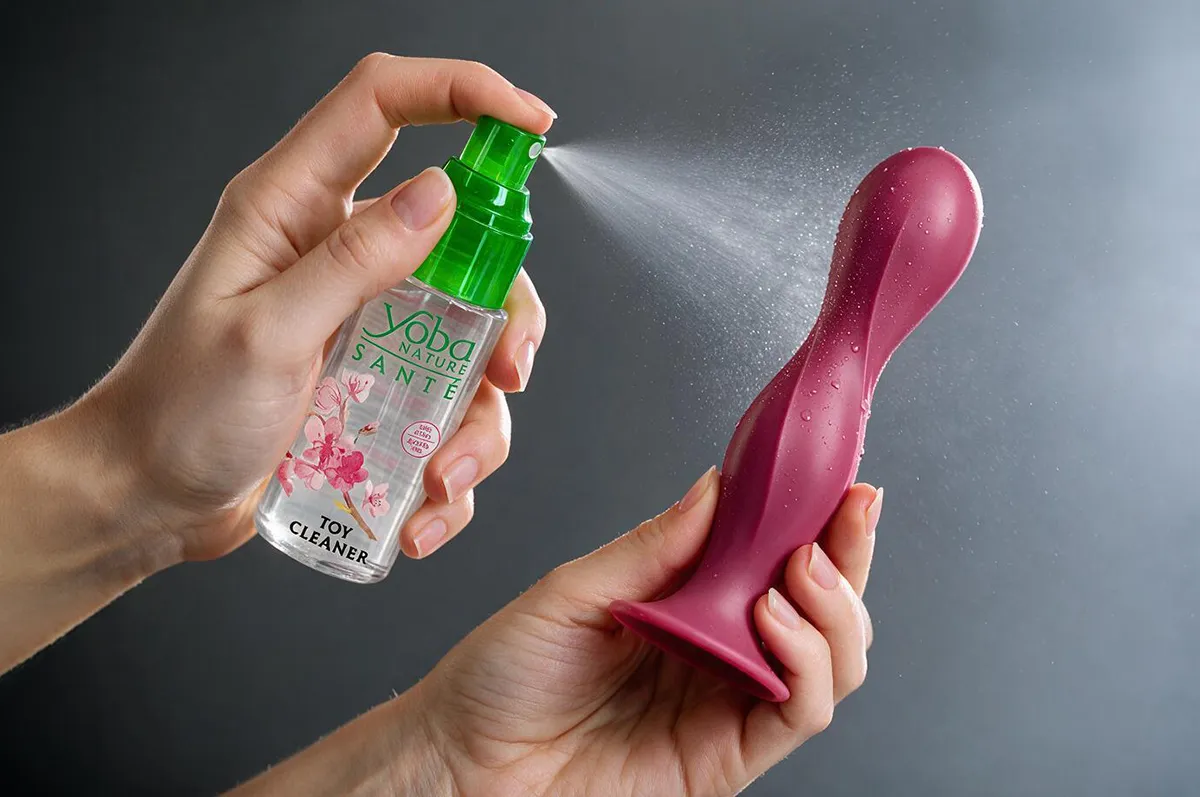 Application d'un nettoyant spécialement conçu pour les sextoys sur un gode en silicone afin d'assurer une hygiène optimale.